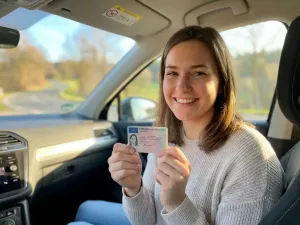 Junge Frau hält frisch ausgestellten deutschen Führerschein in beiden Händen und lächelt stolz im Fahrzeug.
