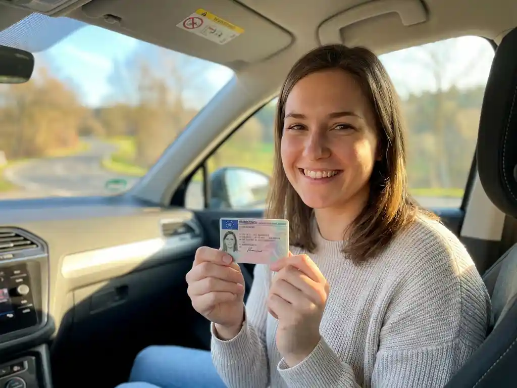 Junge Frau hält frisch ausgestellten deutschen Führerschein in beiden Händen und lächelt stolz im Fahrzeug.