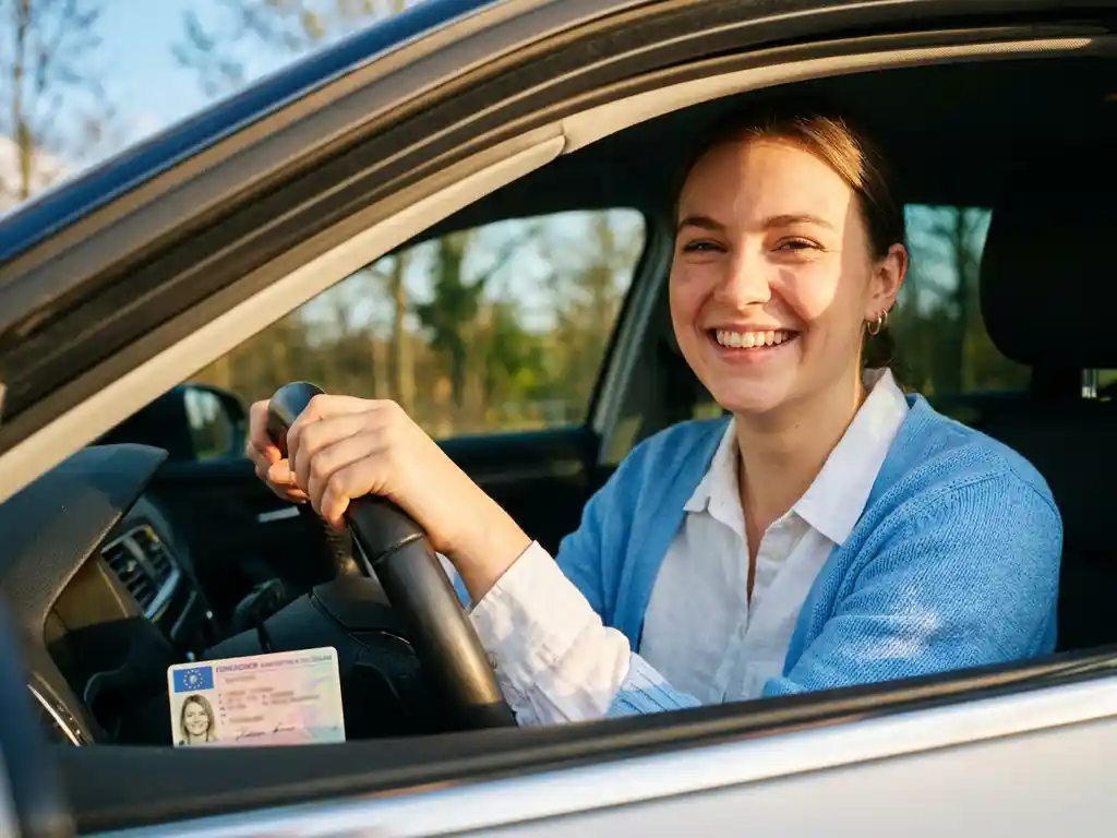 Junge Frau am Steuer eines modernen Autos mit deutschem Führerschein auf dem Armaturenbrett, Sonnenlicht durchflutet den Innenraum.