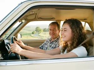 Junge Frau lächelt entspannt am Steuer eines modernen Autos, Fahrlehrer auf Beifahrersitz, grüne deutsche Landschaft im Hintergrund.