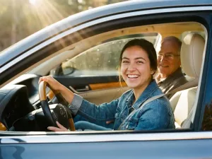 Junge Frau lächelt selbstbewusst am Steuer eines modernen Autos, Fahrlehrer auf dem Beifahrersitz, goldenes Nachmittagslicht.